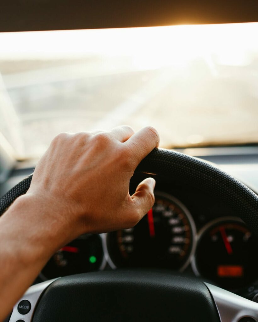 Selective focus man's hand on steering wheel, driving a car at sunset. Travel background.