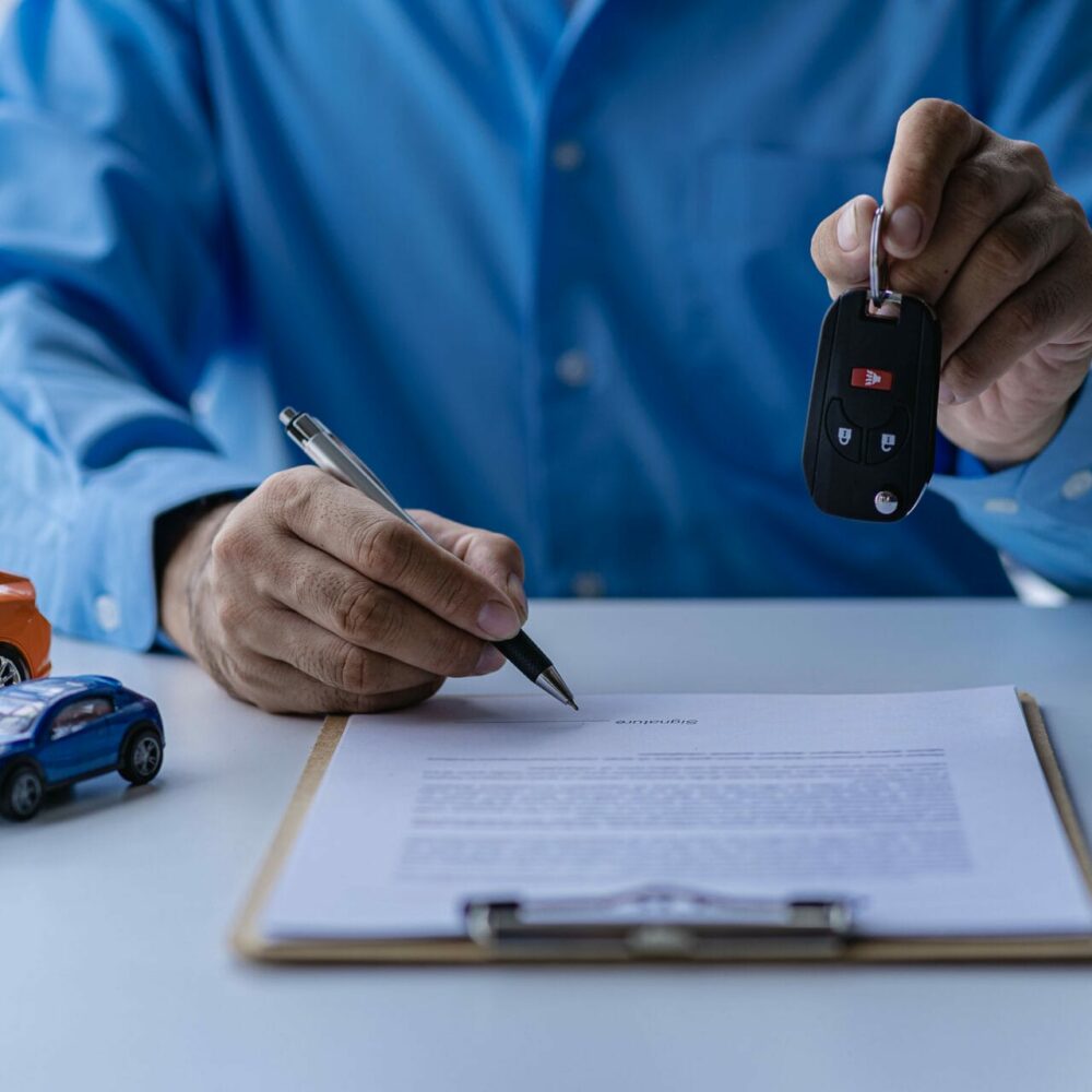 Selling a car. Management concept. The dealer gives the car keys to the new owner or renter with a contract of insurance. Customers who sign the contract and terms of the document